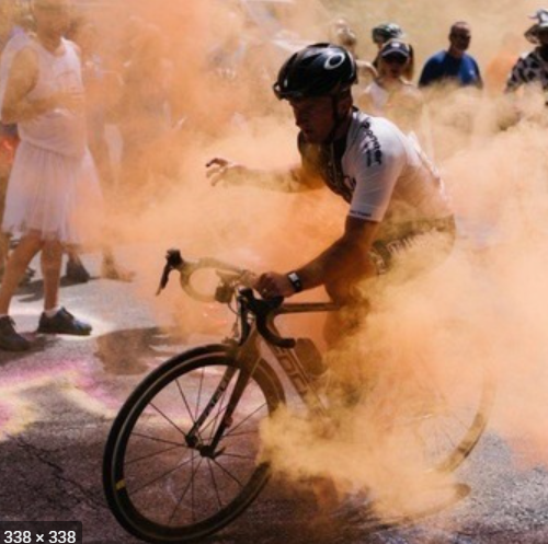 Chad wearing traditional spandex cycling suit with aerodynamic helmet cycling through man-made smoke during a special cycling event.