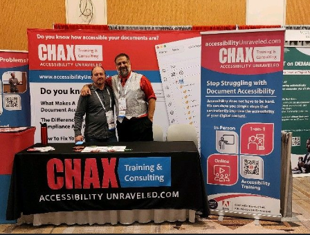 Chad and Dax stand in front of there colorful booth showing two banners a podium and tablecloth with their logo on it.